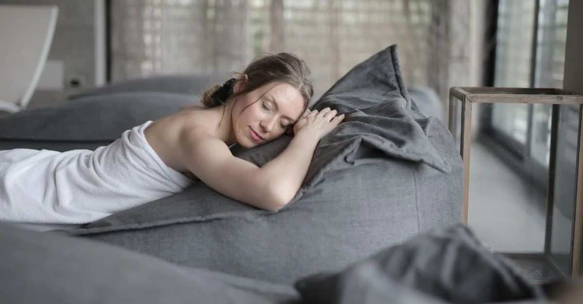 Femme se relaxant paisiblement dans un spa, enveloppée dans une serviette sur un lit confortable, profitant d'une ambiance sereine.
