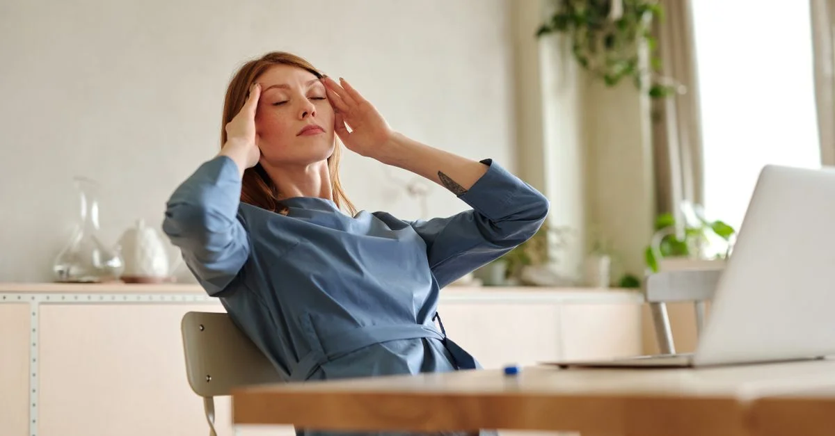 Femme éprouvant du stress au travail, assise à un bureau avec un ordinateur portable, à l'intérieur.