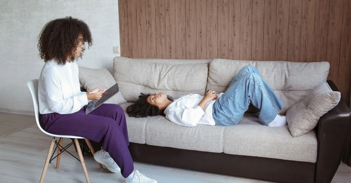 Thérapeute avec une tablette consultant un client allongé sur un sofa lors d'une séance de conseil.