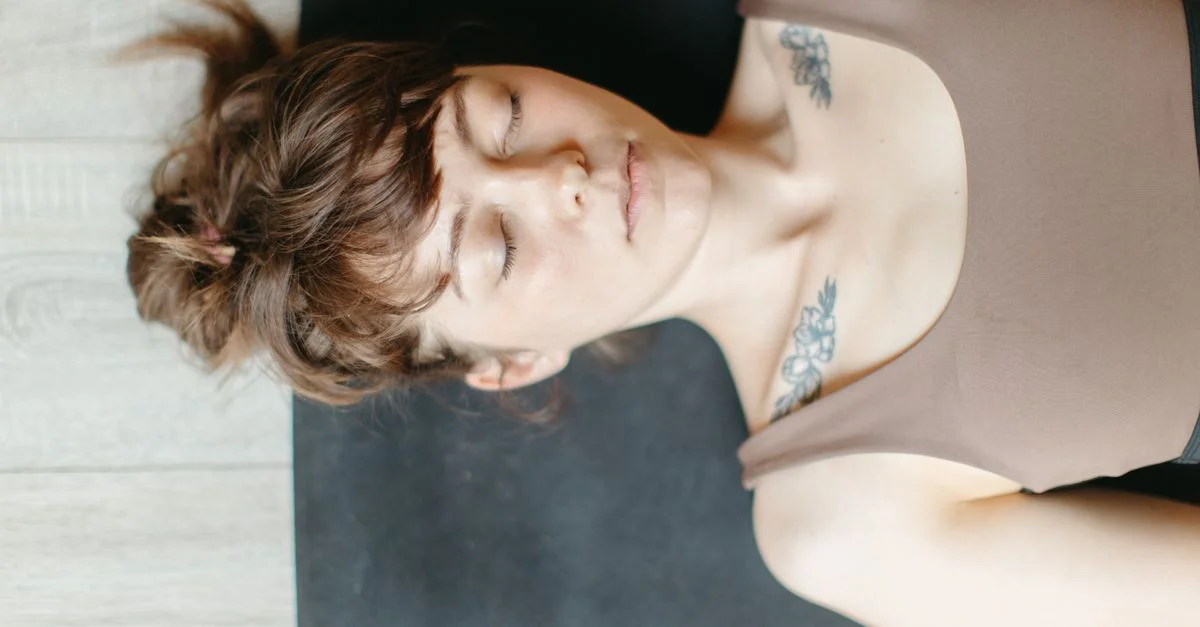 Femme paisible en débardeur se reposant les yeux fermés, mettant en valeur des tatouages