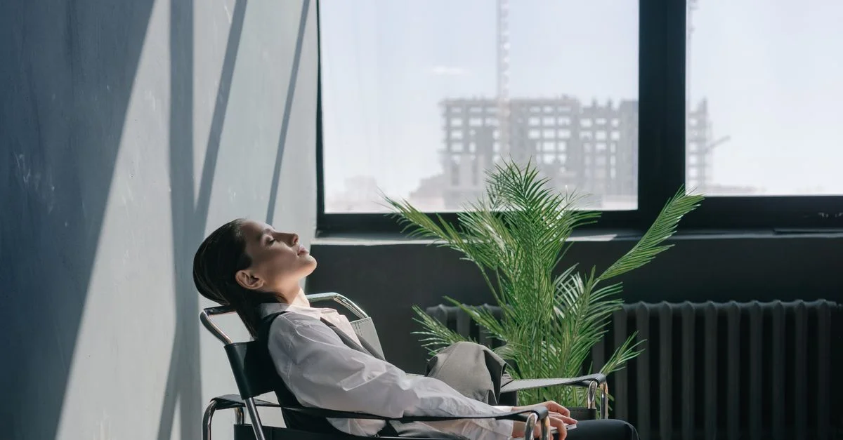 Femme dans un cadre de bureau minimaliste se relaxant près de la fenêtre avec la lumière du soleil qui entre.