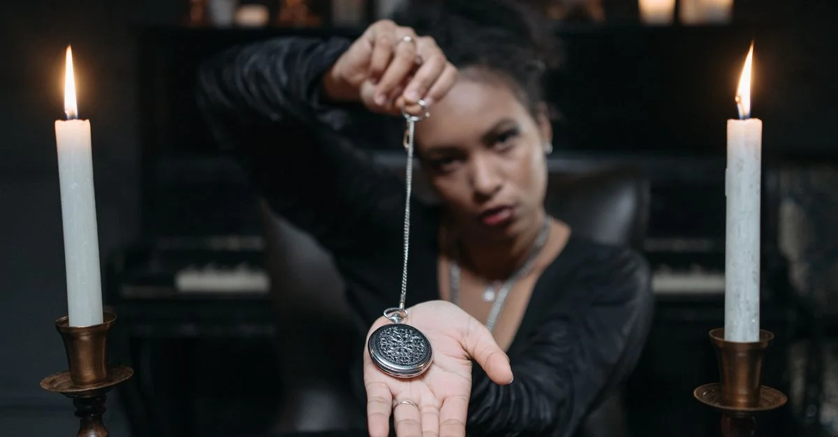 Une femme tenant un pendentif lors d'une séance mystique à la lumière des bougies.