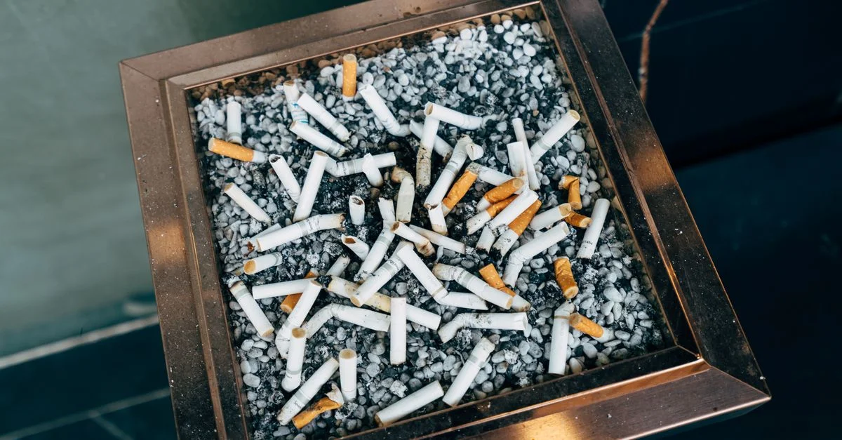 Photo en gros plan de mégots de cigarette dans un cendrier rempli de petits cailloux. Cadre urbain.