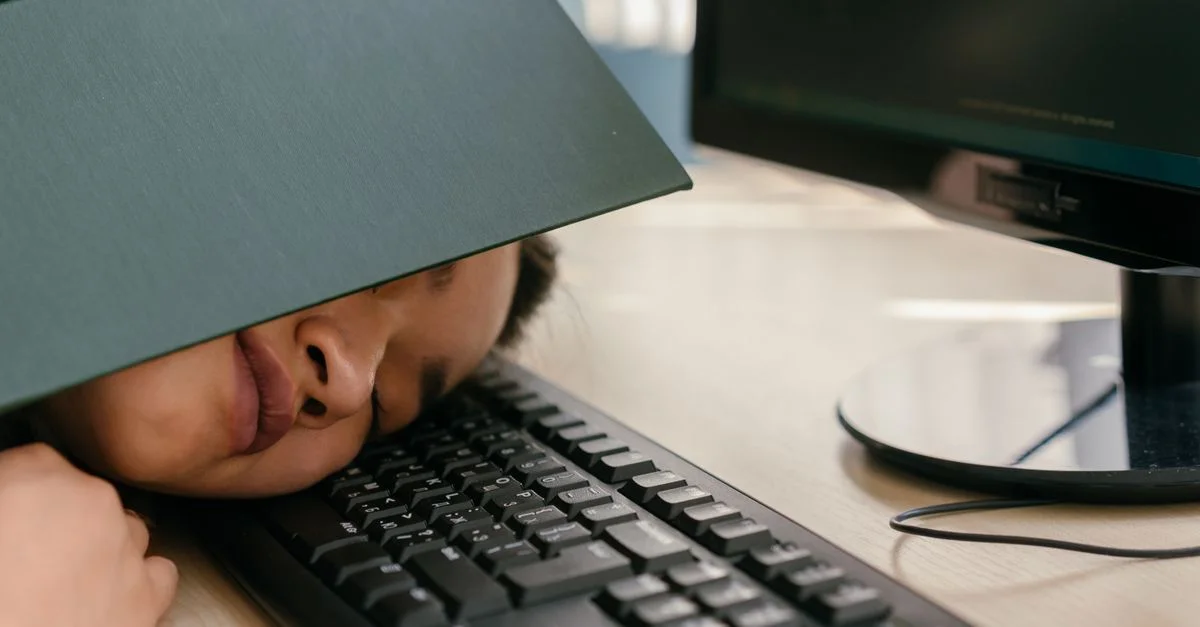 Une jeune femme s'endort sur un clavier avec un manuel posé sur le visage, illustrant la fatigue liée aux études.