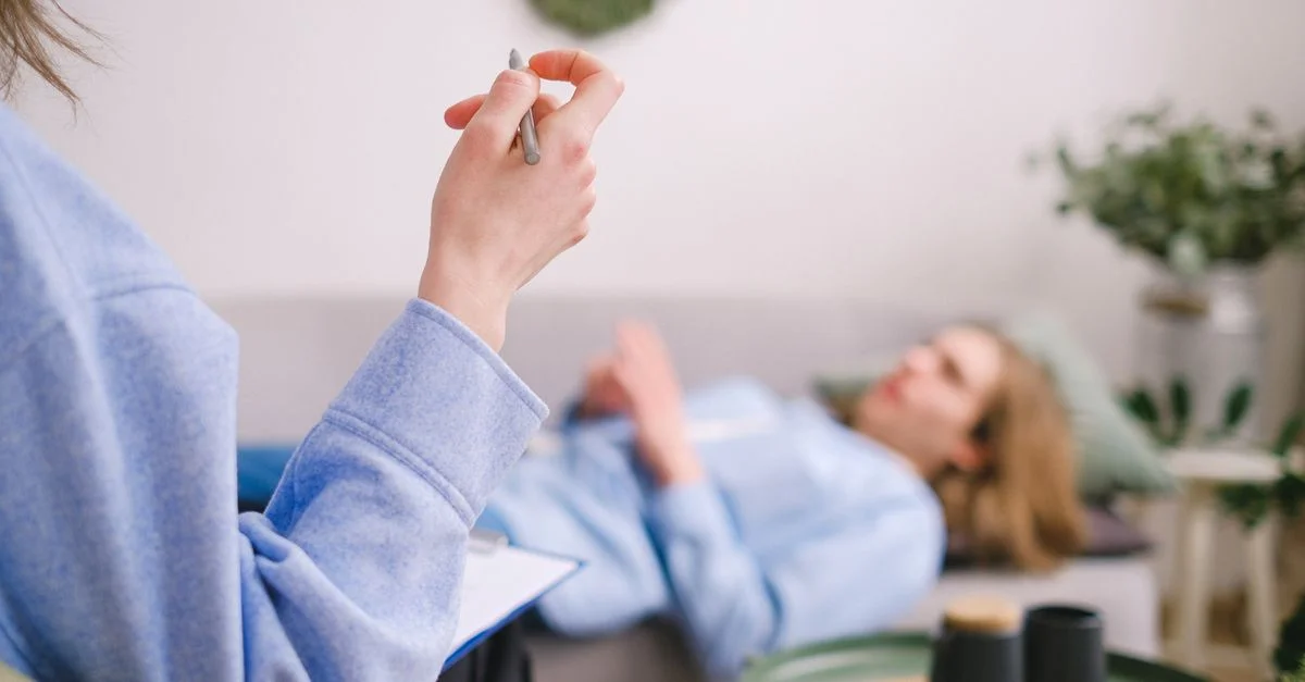 Thérapeute prenant des notes lors d'une séance de thérapie avec un client détendu allongé sur un canapé.