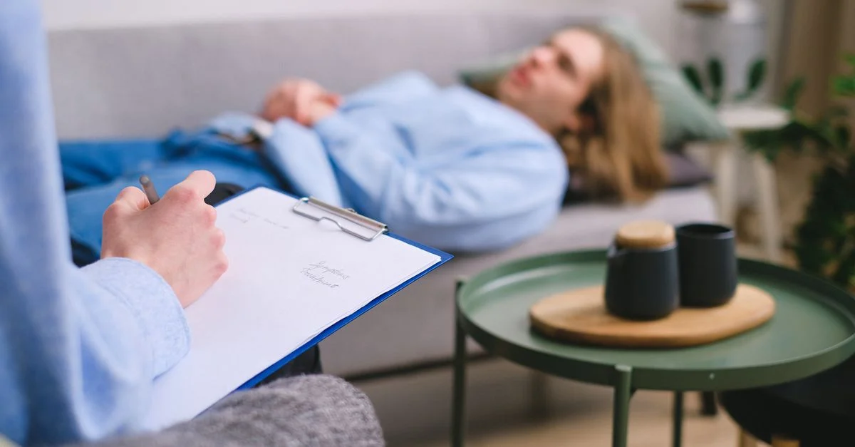 Un thérapeute prenant des notes pendant une séance avec un patient allongé sur un canapé à l'intérieur.
