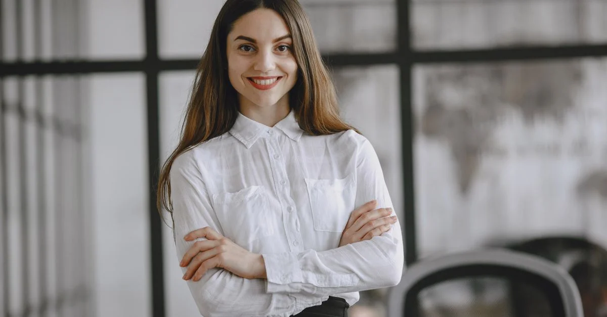 Femme confiante aux cheveux bruns longs, souriante dans un environnement de bureau.