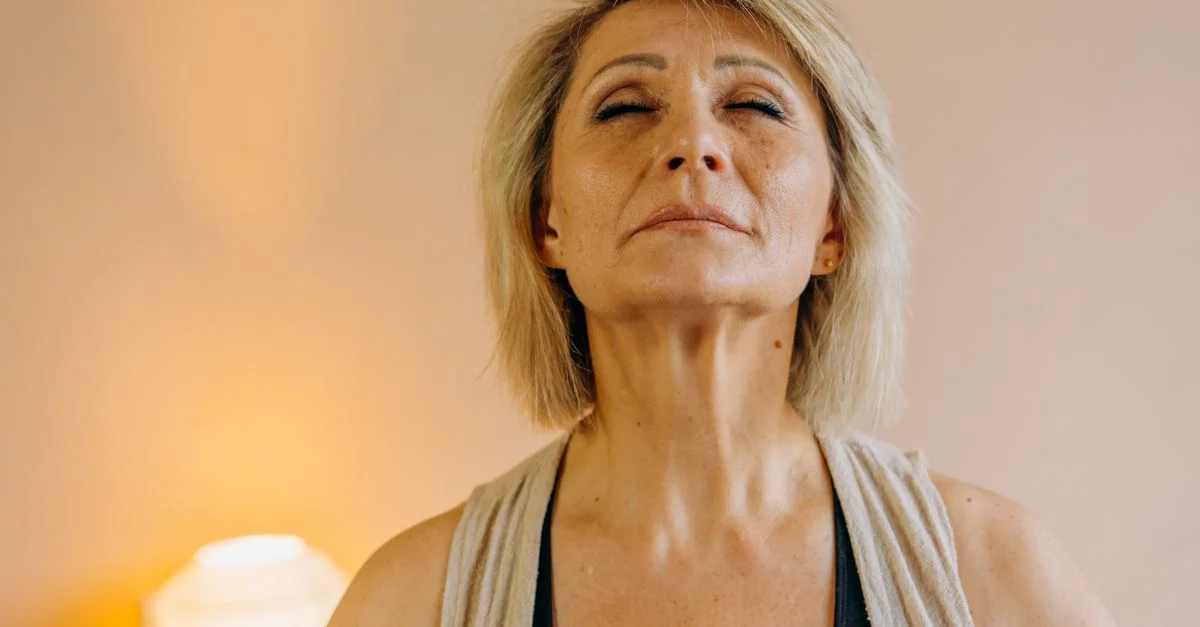 Femme âgée sereine pratiquant la pleine conscience à la maison, les yeux fermés dans un paisible moment de relaxation.