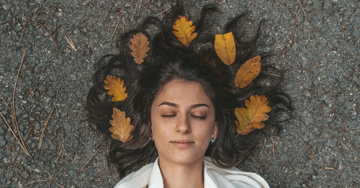 Femme paisible les yeux fermés entourée de feuilles d'automne sur un chemin de gravier à Istanbul.